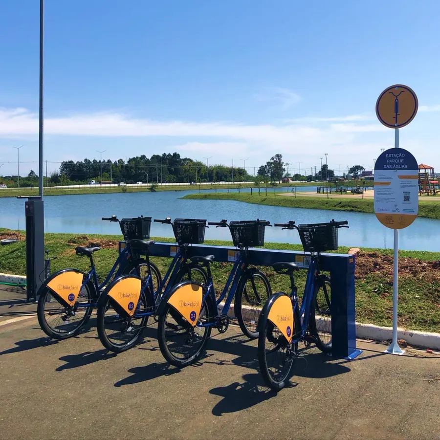 Bicicletas compartilhadas alinhadas em uma estação ao lado de um lago